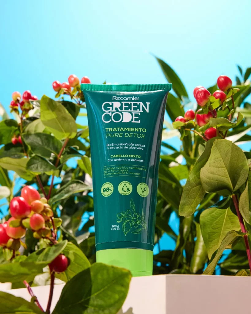 Tube of Recamier Green Code Tratamiento Pure Detox hair treatment, teal packaging with green cap, surrounded by leaves and red berries against a bright blue background.