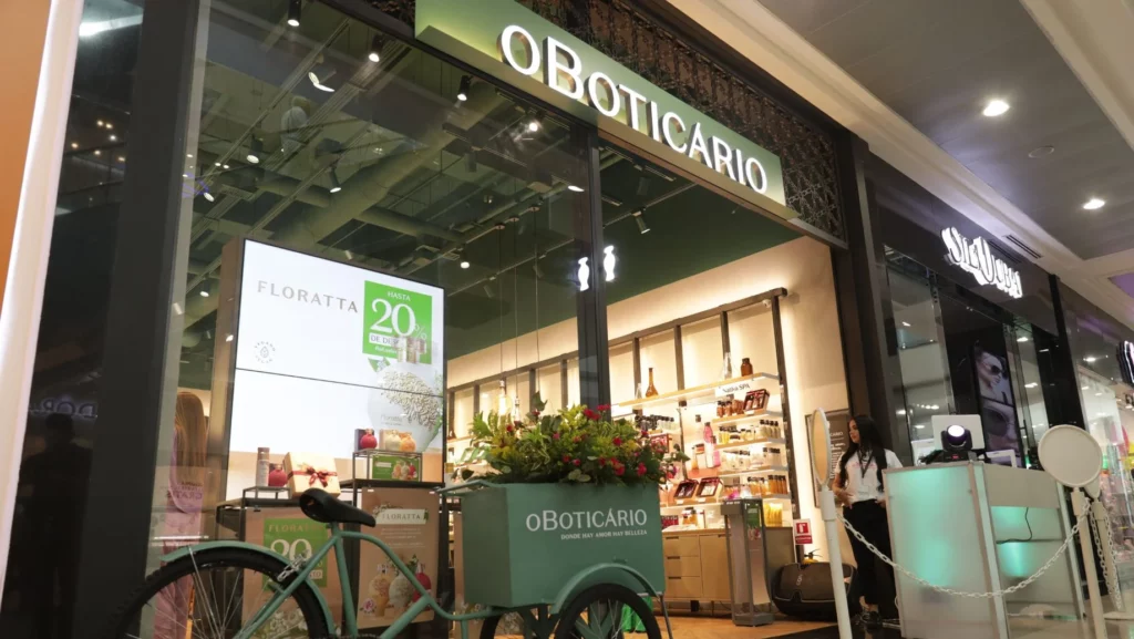 Storefront of O Boticário in a mall, mint-green delivery bike with flowers parked outside and interior shelves visible behind glass door