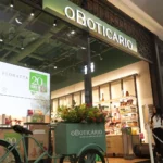 Storefront of O Boticário in a mall, mint-green delivery bike with flowers parked outside and interior shelves visible behind glass door
