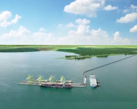 Aerial view of an offshore port with yellow gantry cranes on floating platforms and a docked cargo ship connected by a pier.