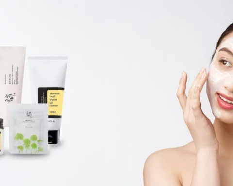 Smiling woman applying cream to her face beside a row of skincare products on a white surface.