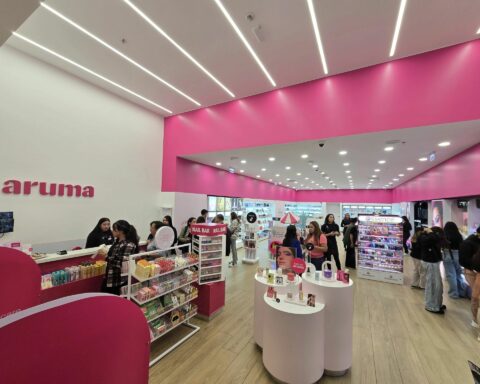 Bright cosmetics store interior with pink walls, white counters, circular display plinths, and customers browsing makeup products.