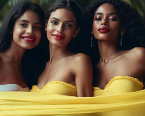 Three women posing together outdoors, smiling and wearing yellow strapless tops with a yellow scarf around them.