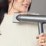Woman holding a hair dryer in a gray advertisement banner, with white text: 'SAGITTA Potencia inteligente para un acabado superior' and a neon yellow 'LÍNEA PROFESIONAL' badge.