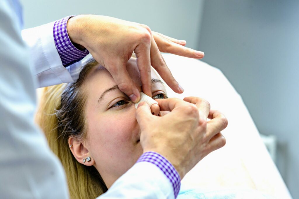 Medical professional inserts nasal gauze into a patient’s nostril during a procedure, patient lying down.