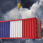Shipping container painted in blue, white, and red being lifted by a crane against a dark stormy sky.