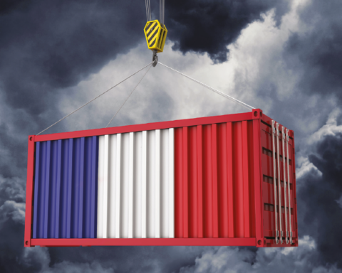 Shipping container painted in blue, white, and red being lifted by a crane against a dark stormy sky.