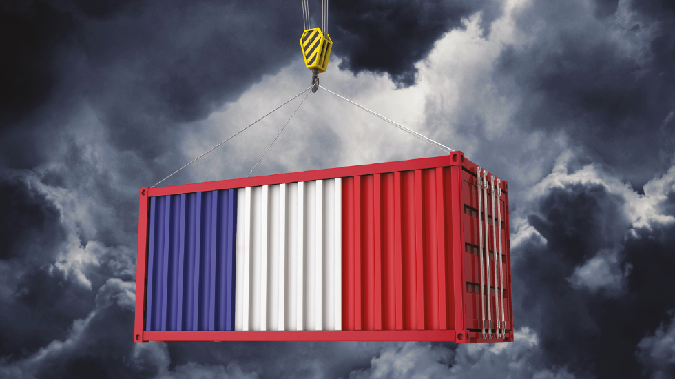 Shipping container painted in blue, white, and red being lifted by a crane against a dark stormy sky.