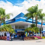 Blue Farmatodo storefront with palm trees and a clear sky, customers outside the entrance on a sunny day