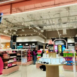 Bright cosmetics shop interior with a pink curved entrance, shelves of products, and a circular display table in the center as shoppers browse the aisles.