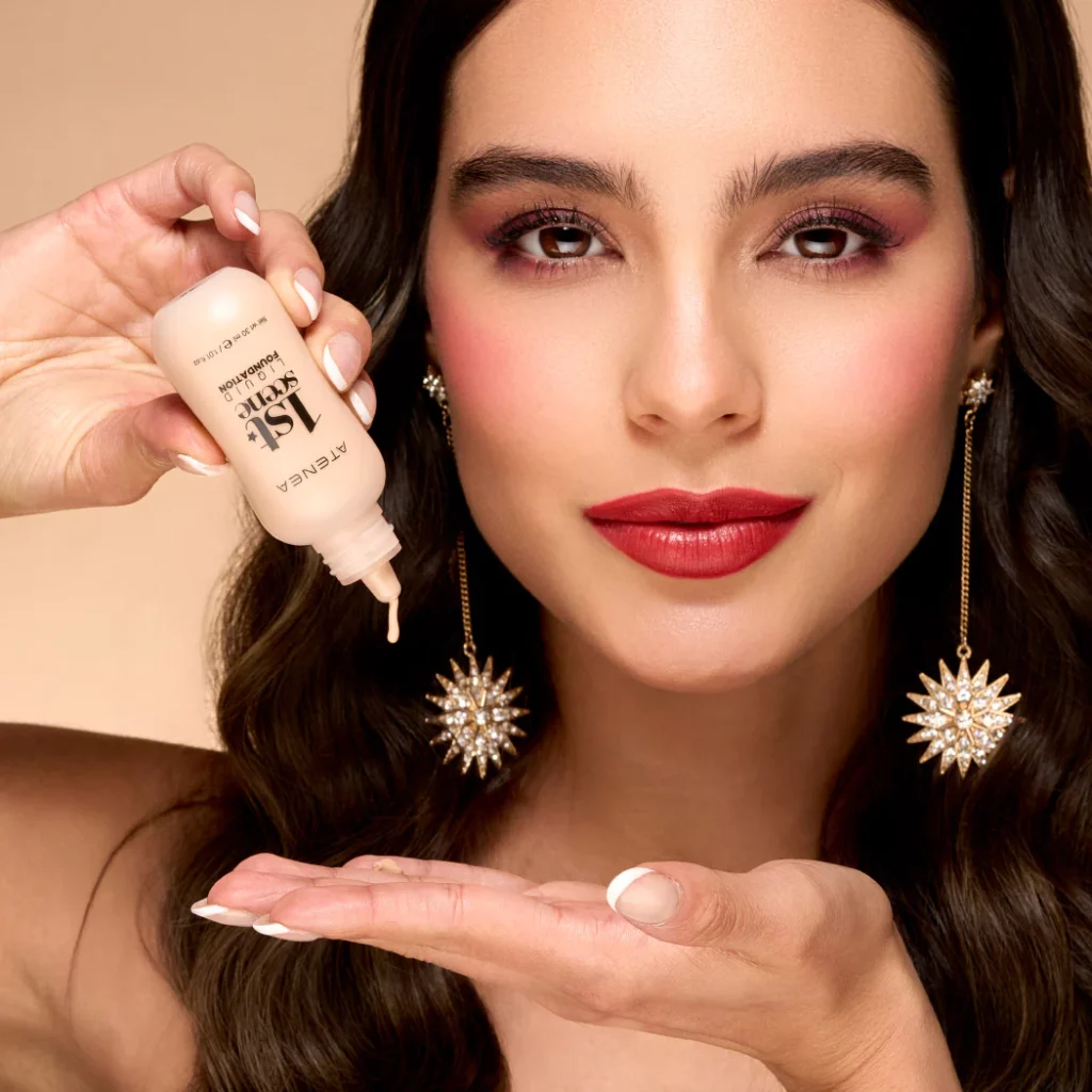 Close-up of a woman applying serum from a dropper bottle near her face, with bold makeup and statement earrings.