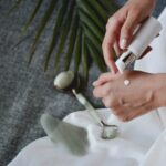 Person applying white cream to the back of their hand from a pump bottle on a fabric background in a skincare routine.