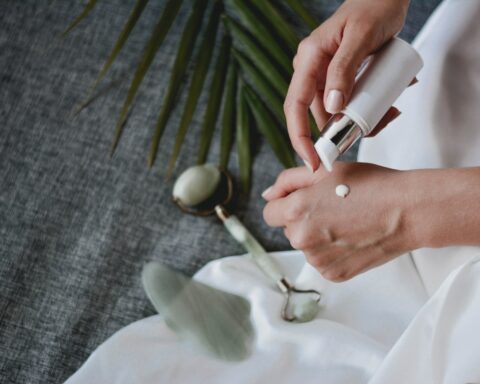 Person applying white cream to the back of their hand from a pump bottle on a fabric background in a skincare routine.