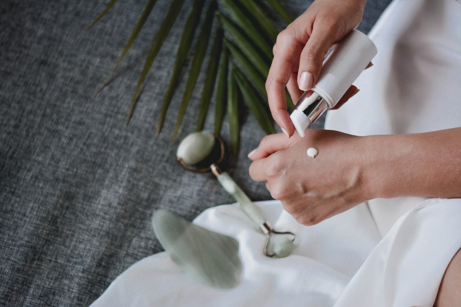 Person applying white cream to the back of their hand from a pump bottle on a fabric background in a skincare routine.